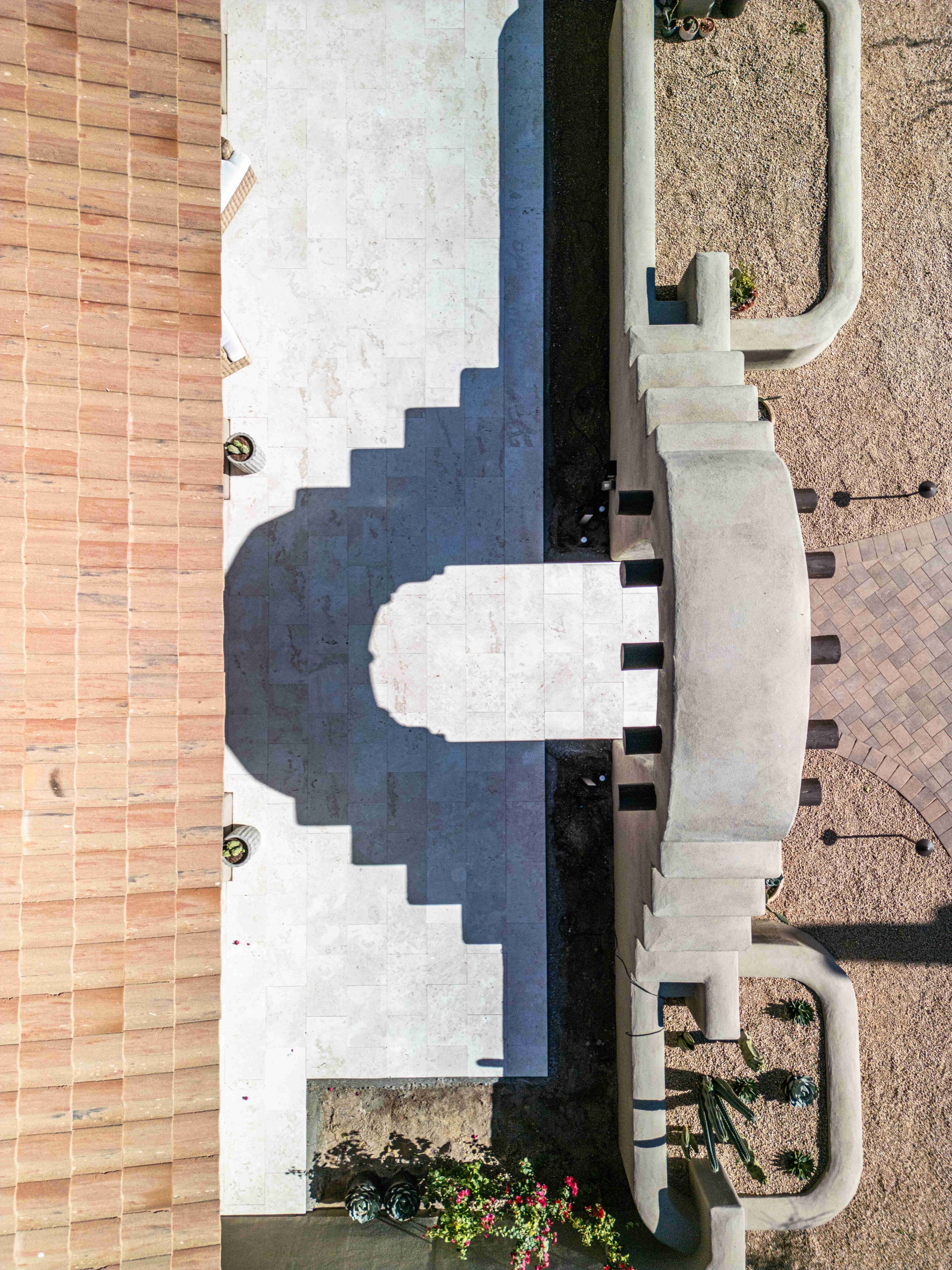 Aerial view of a travertine courtyard and arched stucco entry with a paver driveway beyond